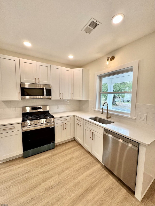 kitchen with light hardwood / wood-style floors, white cabinetry, sink, and stainless steel appliances