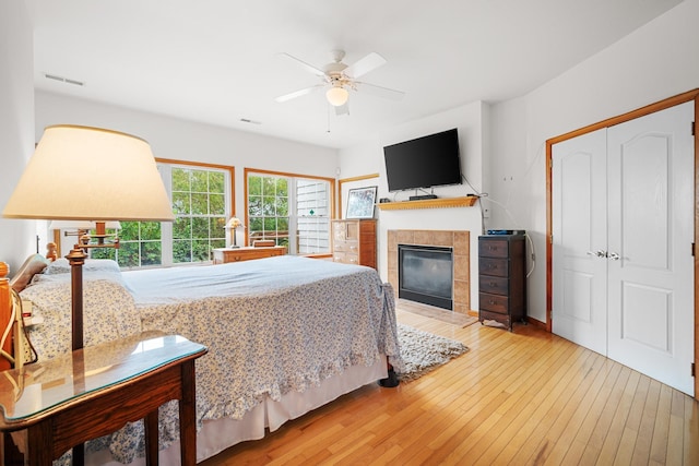 bedroom featuring wood-type flooring, a closet, a tiled fireplace, and ceiling fan