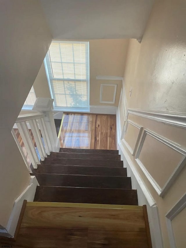 stairway with wainscoting, wood finished floors, and a decorative wall