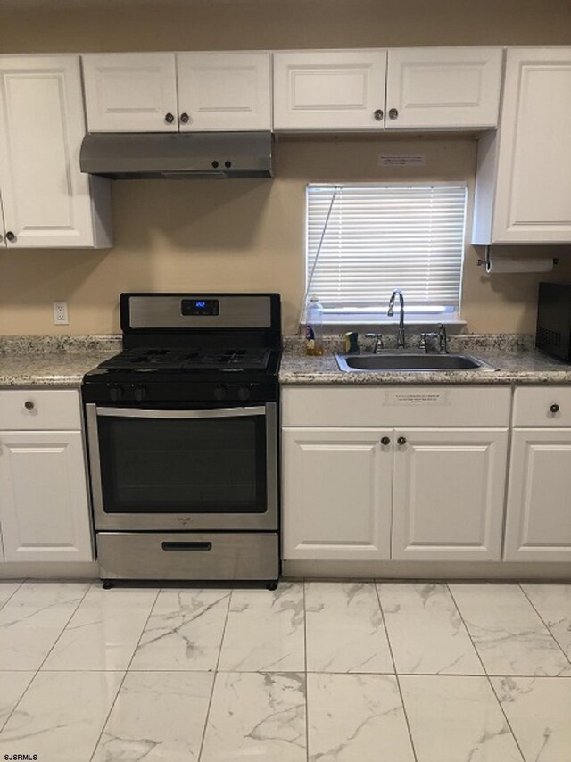 kitchen featuring marble finish floor, stainless steel range with gas cooktop, under cabinet range hood, white cabinetry, and a sink