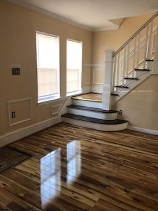 interior space featuring a decorative wall, crown molding, baseboards, wood finished floors, and stairway