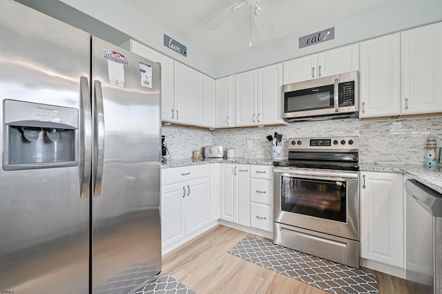 kitchen featuring light stone counters, white cabinets, stainless steel appliances, ceiling fan, and light hardwood / wood-style flooring