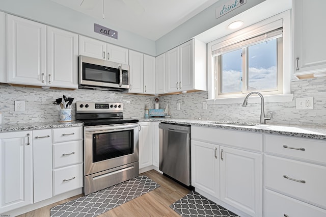 kitchen featuring appliances with stainless steel finishes, light hardwood / wood-style floors, tasteful backsplash, white cabinets, and sink