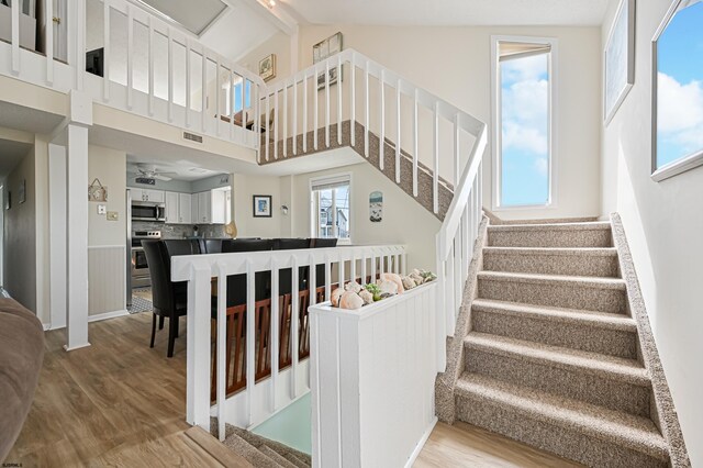 staircase featuring high vaulted ceiling, beam ceiling, ceiling fan, and hardwood / wood-style flooring