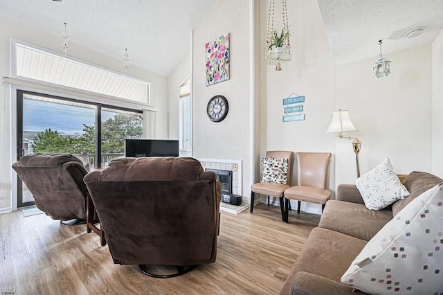 living room featuring light wood-type flooring, a textured ceiling, a fireplace, and vaulted ceiling