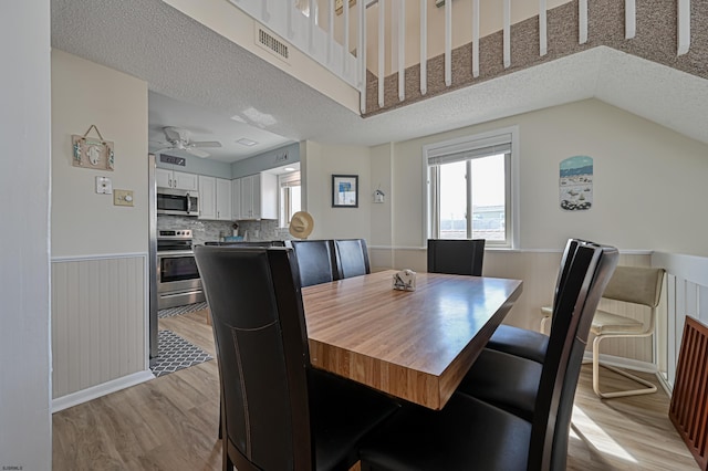 dining space with ceiling fan, a textured ceiling, light wood-type flooring, and lofted ceiling