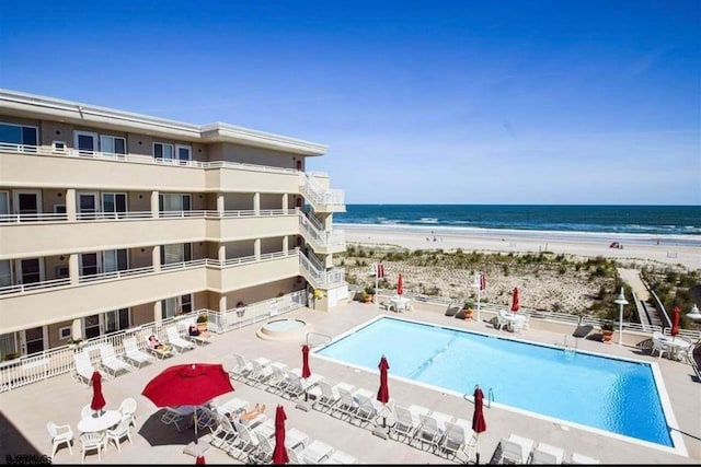 view of swimming pool featuring a water view, a beach view, and a patio area