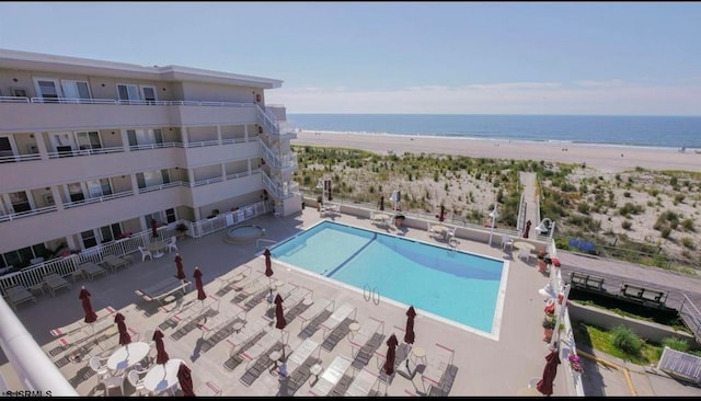 view of swimming pool with a water view, a beach view, and a patio area