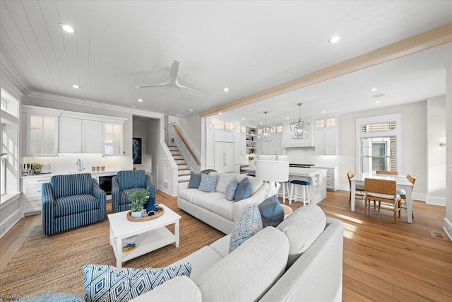 living room featuring ceiling fan with notable chandelier, sink, light hardwood / wood-style flooring, and crown molding