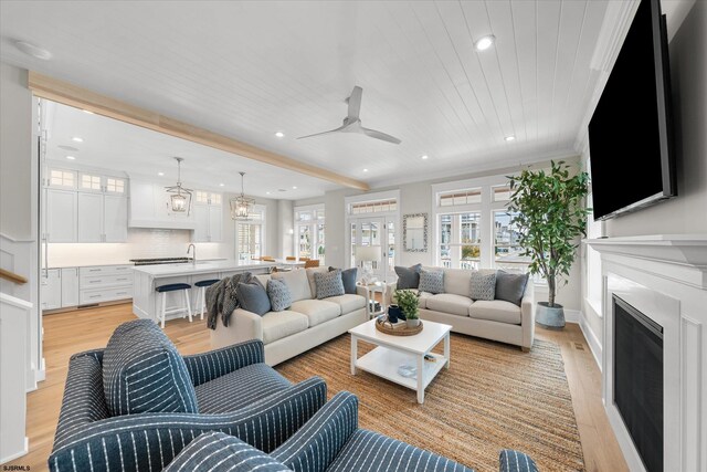 living room with ceiling fan with notable chandelier, wooden ceiling, crown molding, light hardwood / wood-style flooring, and sink