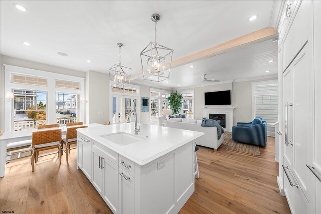 kitchen featuring a kitchen island with sink, sink, white cabinetry, light hardwood / wood-style flooring, and decorative light fixtures