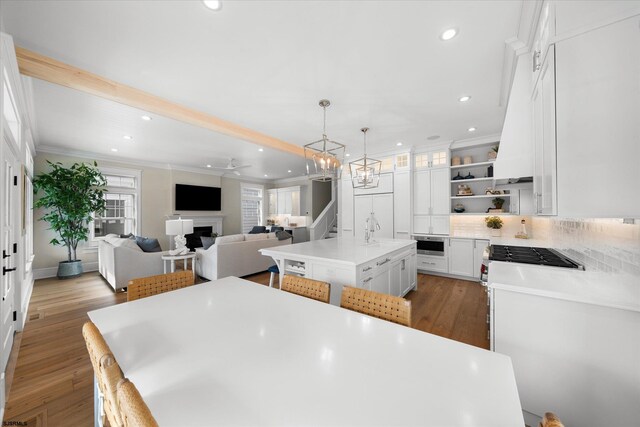 kitchen featuring dark wood-type flooring, a kitchen island with sink, white cabinets, hanging light fixtures, and ornamental molding