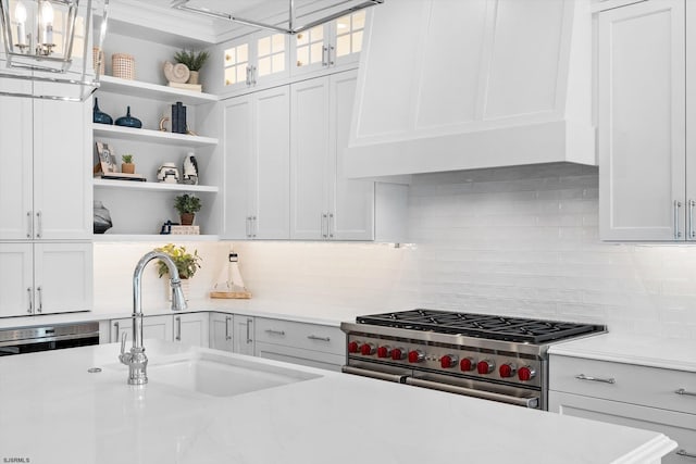 kitchen with tasteful backsplash, white cabinets, high end stove, pendant lighting, and sink