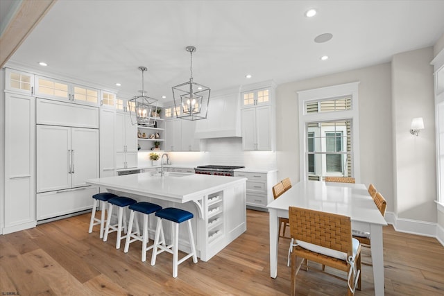 kitchen with white cabinets, light wood-type flooring, a kitchen island with sink, and sink