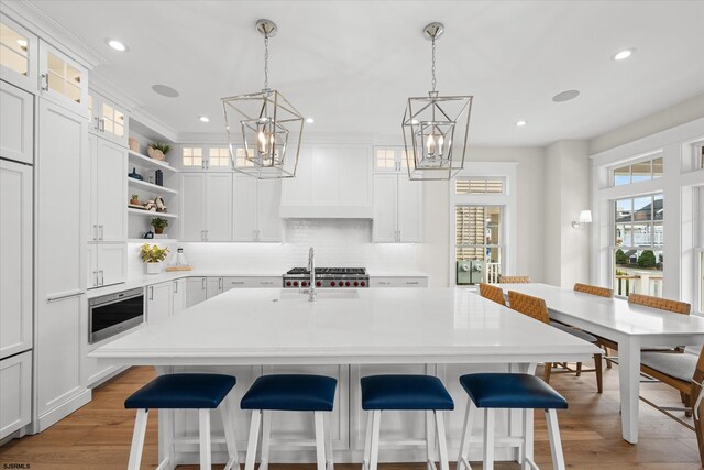 kitchen featuring custom exhaust hood, an island with sink, light hardwood / wood-style flooring, a chandelier, and white cabinetry