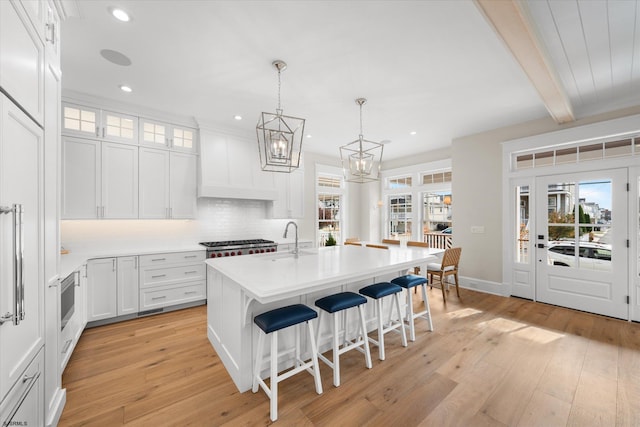 kitchen with white cabinets, light wood-type flooring, beam ceiling, and a healthy amount of sunlight