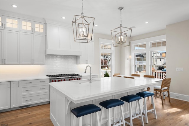 kitchen featuring light wood-type flooring, a kitchen island with sink, white cabinetry, and sink