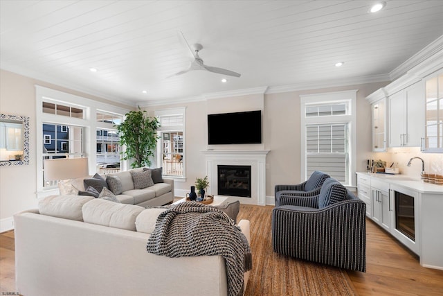 living room with light hardwood / wood-style floors, beverage cooler, ceiling fan, ornamental molding, and sink