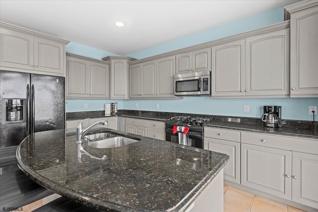 kitchen with a center island with sink, light tile patterned flooring, black appliances, dark stone counters, and sink