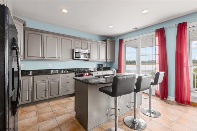 kitchen featuring dark stone counters, a kitchen island with sink, sink, stainless steel appliances, and a water view