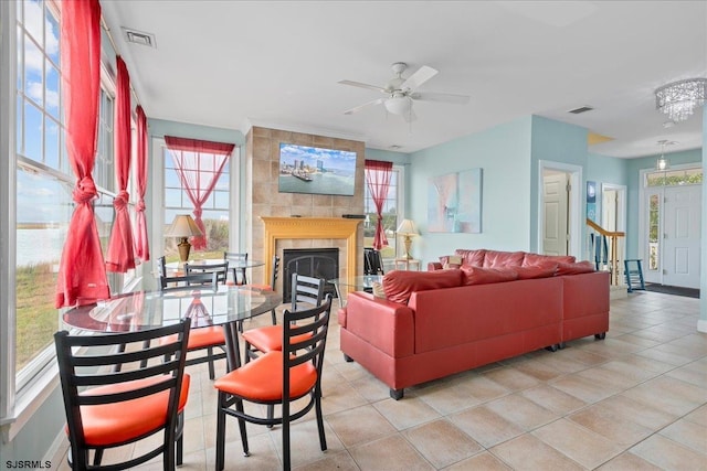 tiled living room featuring ceiling fan with notable chandelier, a tiled fireplace, and a healthy amount of sunlight