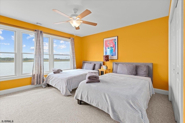 carpeted bedroom with a water view, ceiling fan, and a closet