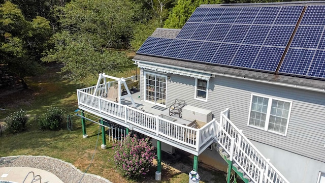 back of property with a wooden deck, solar panels, and a lawn