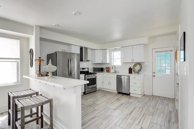 kitchen with white cabinets, kitchen peninsula, wall chimney exhaust hood, stainless steel appliances, and a breakfast bar area