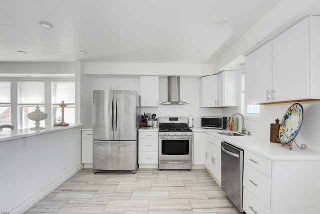 kitchen with a healthy amount of sunlight, stainless steel appliances, wall chimney range hood, and white cabinetry