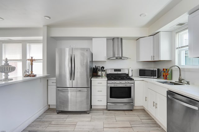 kitchen with appliances with stainless steel finishes, wall chimney exhaust hood, white cabinetry, and sink