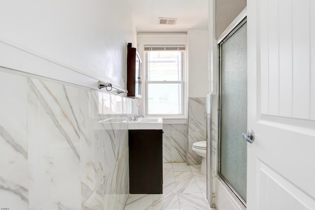 full bathroom with tile walls, bath / shower combo with glass door, vanity, and toilet