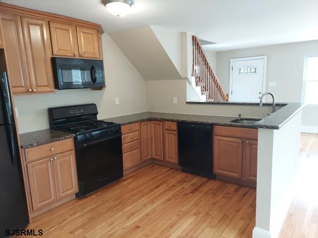 kitchen with dark stone countertops, black appliances, kitchen peninsula, and light wood-type flooring