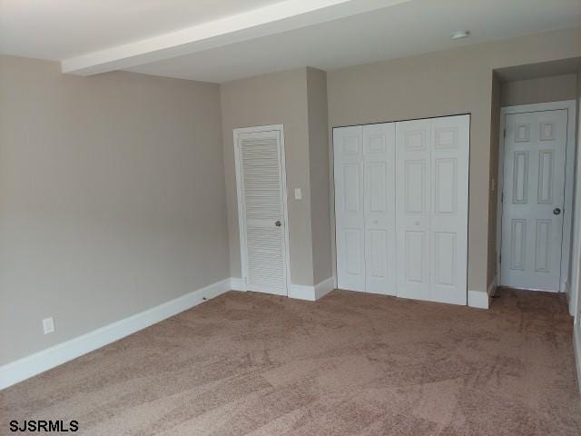 unfurnished bedroom featuring light carpet and beamed ceiling