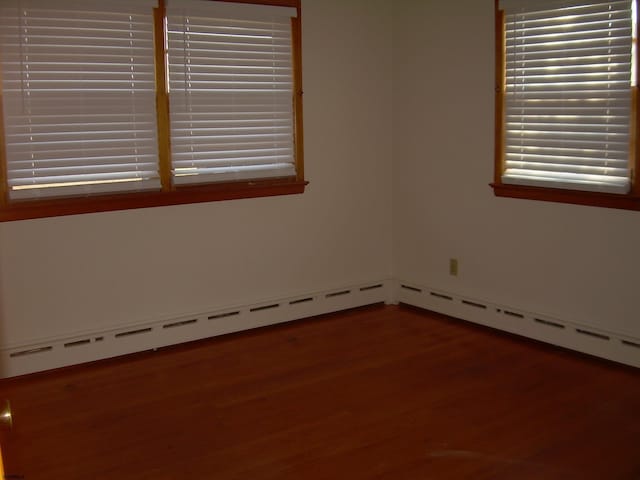 unfurnished room with wood-type flooring and baseboard heating