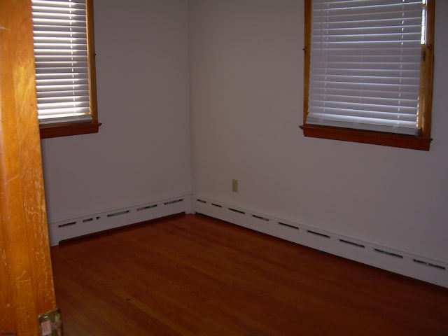 empty room with dark hardwood / wood-style floors and a baseboard heating unit