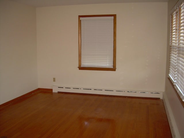 empty room with hardwood / wood-style flooring and a baseboard heating unit