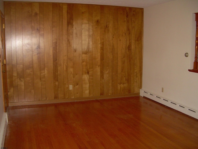 empty room featuring wood-type flooring, wooden walls, and baseboard heating