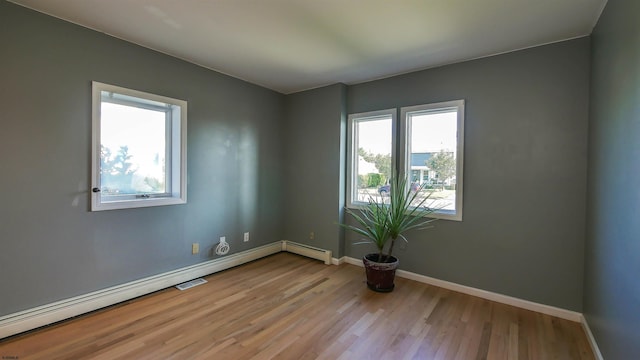 empty room featuring baseboard heating, light hardwood / wood-style flooring, and plenty of natural light