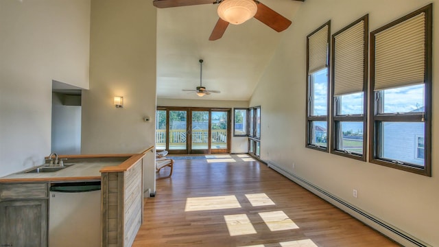 interior space featuring a baseboard radiator, light wood-type flooring, sink, and high vaulted ceiling