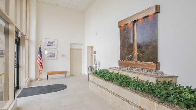 interior space featuring a paneled ceiling, tile patterned flooring, a towering ceiling, and baseboards