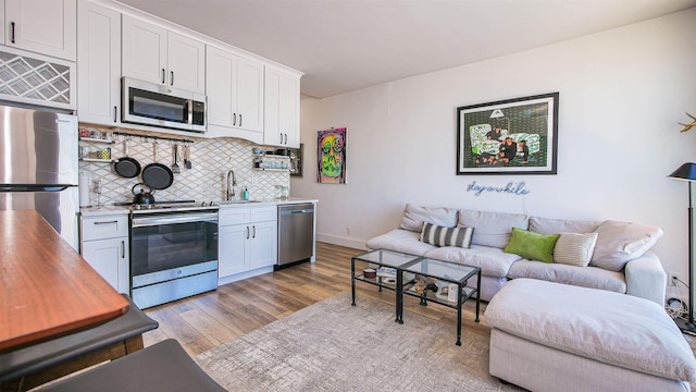 kitchen featuring light wood finished floors, stainless steel appliances, light countertops, decorative backsplash, and white cabinetry