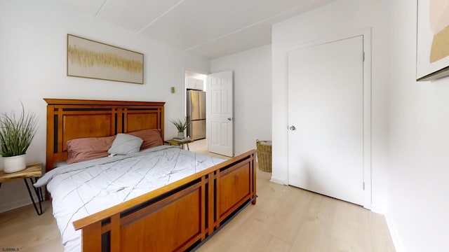 bedroom with stainless steel refrigerator and light hardwood / wood-style floors