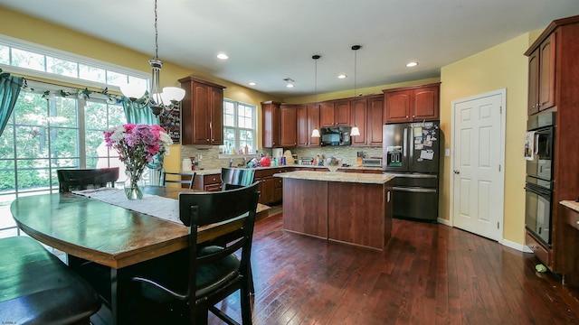 kitchen featuring hanging light fixtures, backsplash, a kitchen island, dark hardwood / wood-style flooring, and black appliances