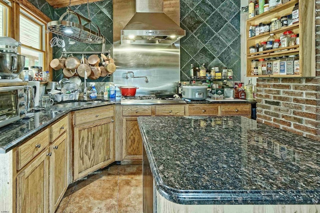 kitchen featuring stainless steel gas stovetop, dark stone countertops, and wall chimney range hood