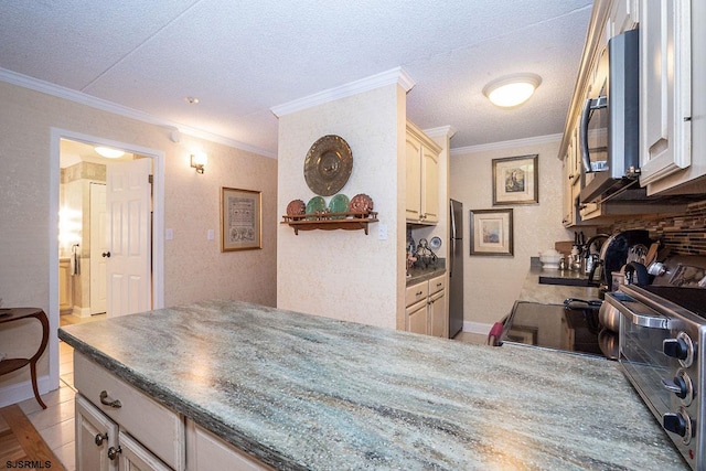 kitchen with a textured ceiling, sink, appliances with stainless steel finishes, ornamental molding, and cream cabinets