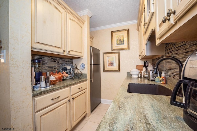 kitchen featuring dark stone counters, light tile patterned flooring, sink, stainless steel refrigerator, and ornamental molding