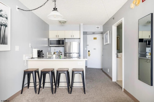 kitchen featuring a textured ceiling, hanging light fixtures, kitchen peninsula, and stainless steel appliances