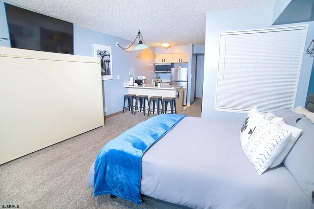 carpeted bedroom featuring a textured ceiling and stainless steel refrigerator