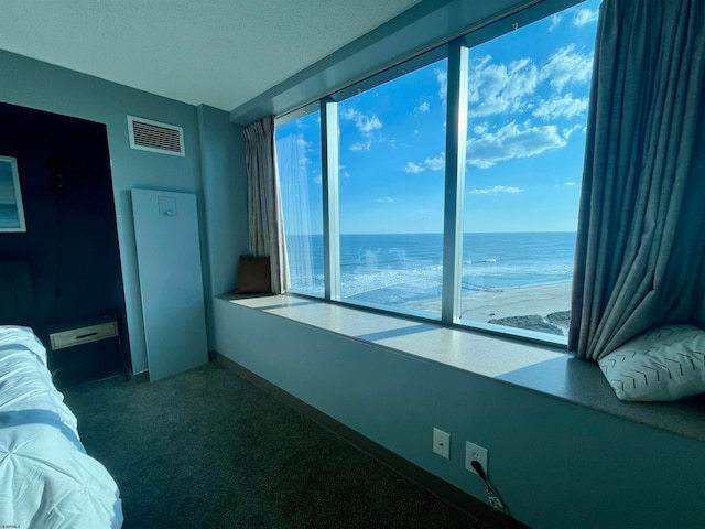 interior space featuring a textured ceiling, a view of the beach, a water view, and carpet floors