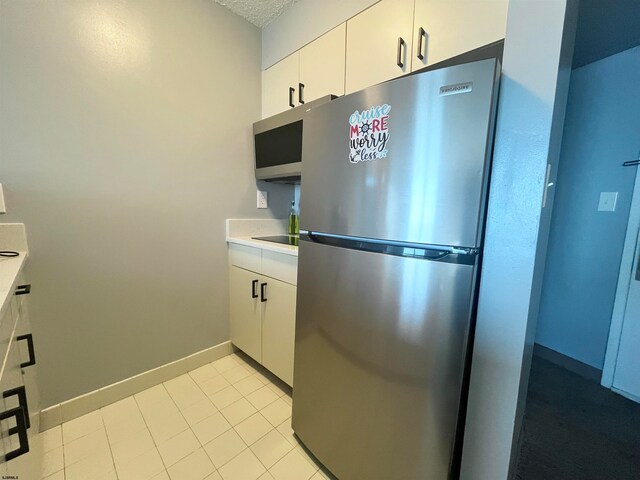 kitchen with a textured ceiling, appliances with stainless steel finishes, light tile patterned floors, and white cabinetry